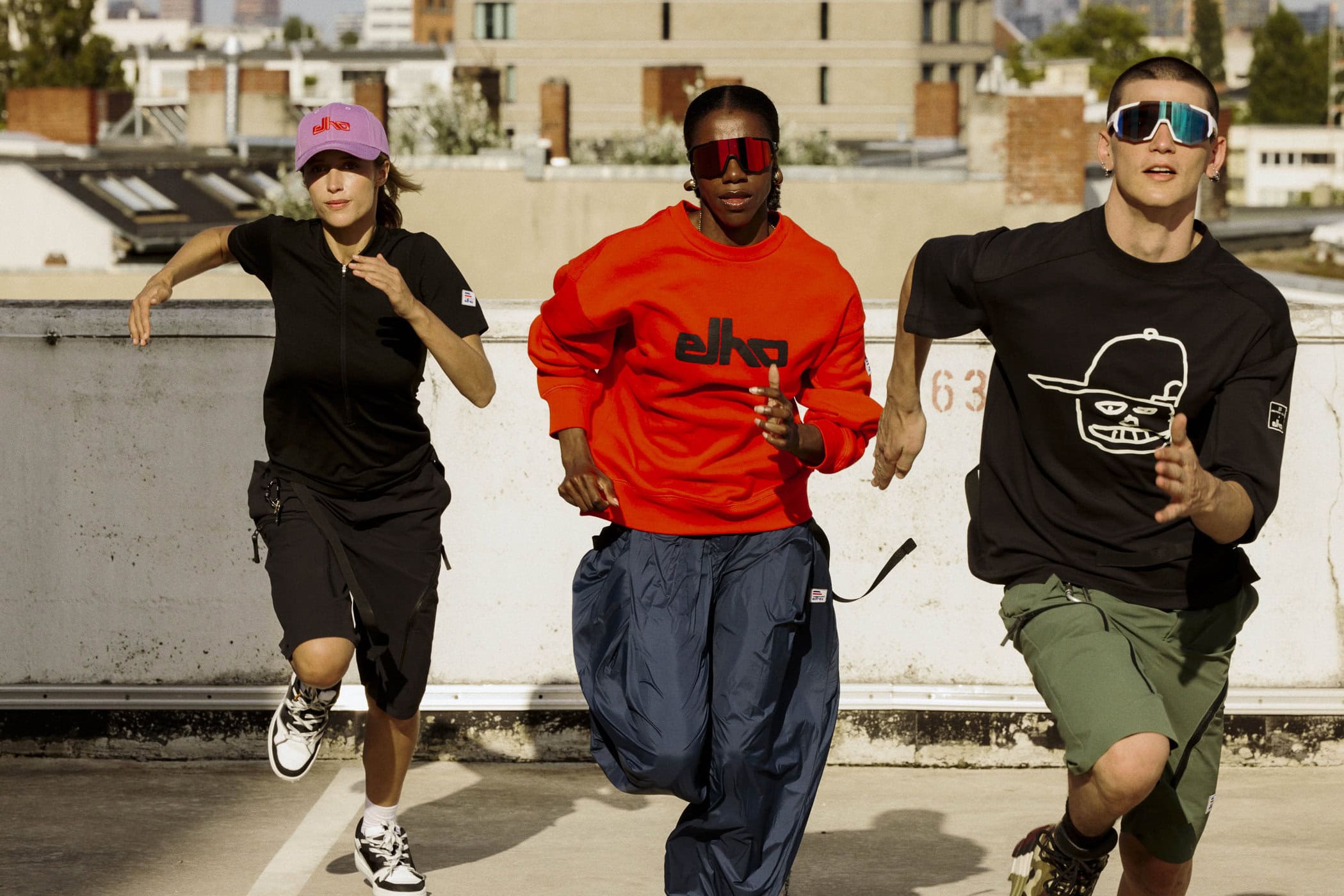 Three models running across a concrete rooftop wearing Elho sportswear apparel and sunglasses.