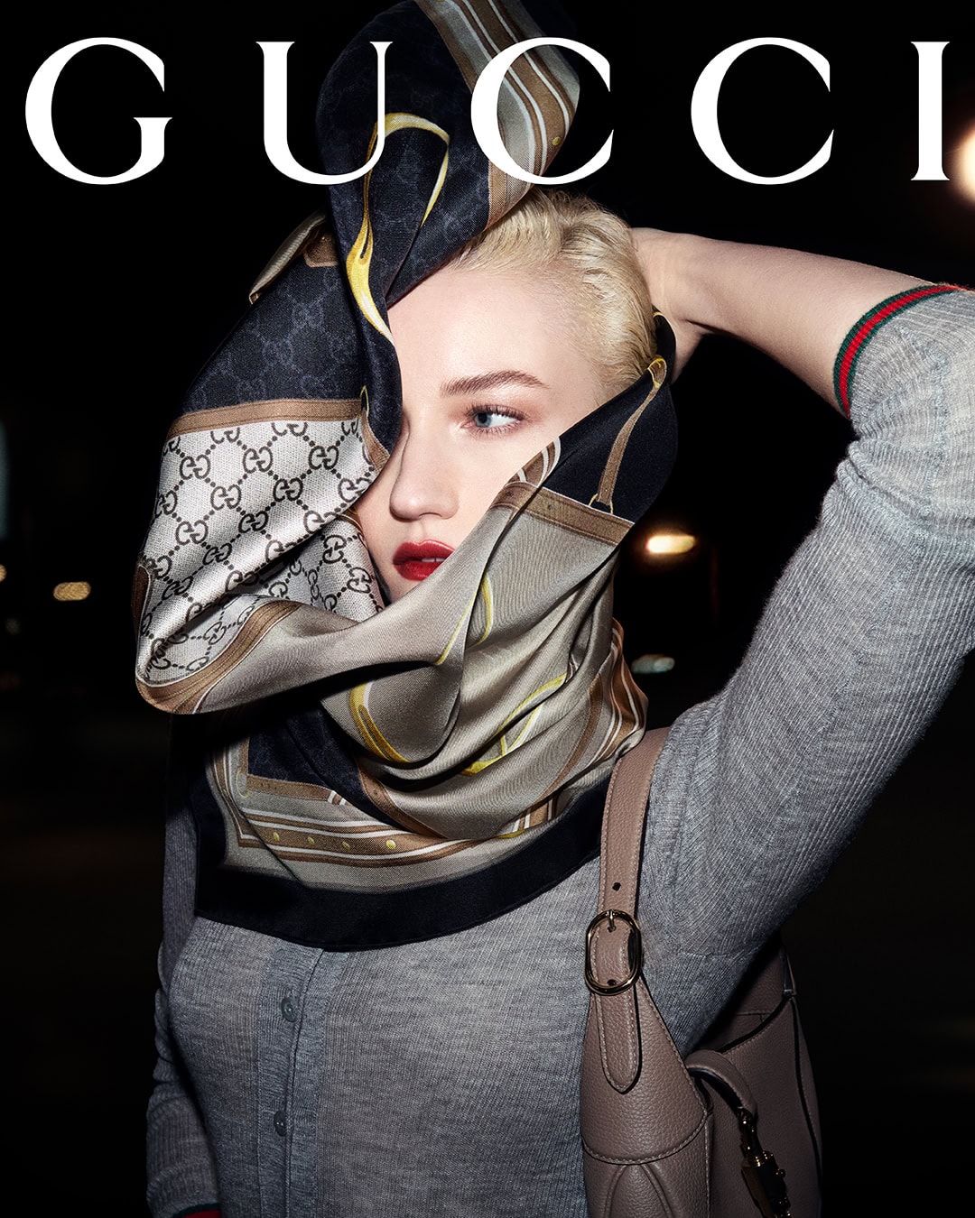 Model wearing a monogram silk scarf over her face and a grey cardigan for Gucci