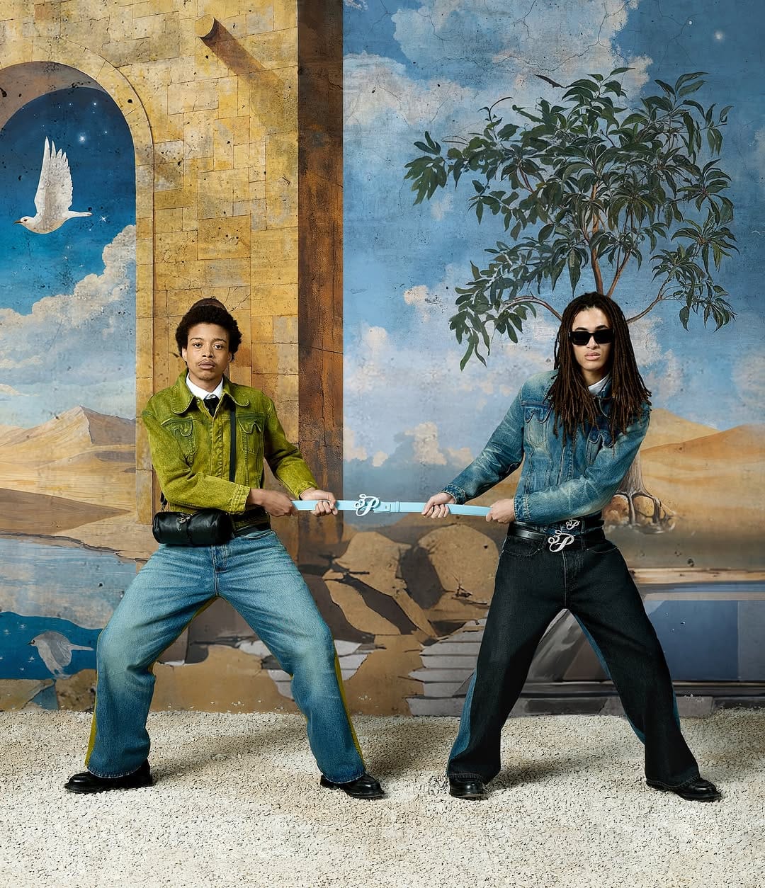 Two models pulling a blue strap against a painted backdrop of a classical architectural landscape