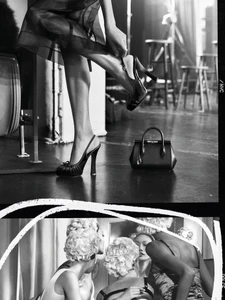 Black and white editorial image of a model putting on a high heel shoe with a handbag resting on the floor nearby