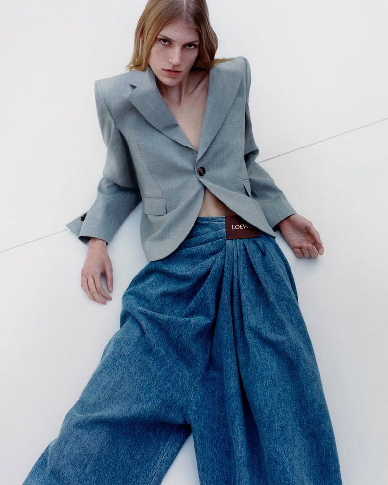 Model in a grey structured blazer and loose blue denim trousers against a white background