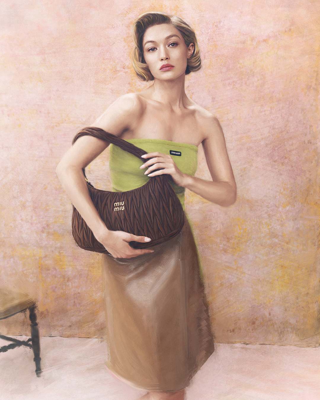 Gigi Hadid posing against a textured pink backdrop wearing a green top and brown skirt while holding a brown Miu Miu handbag.