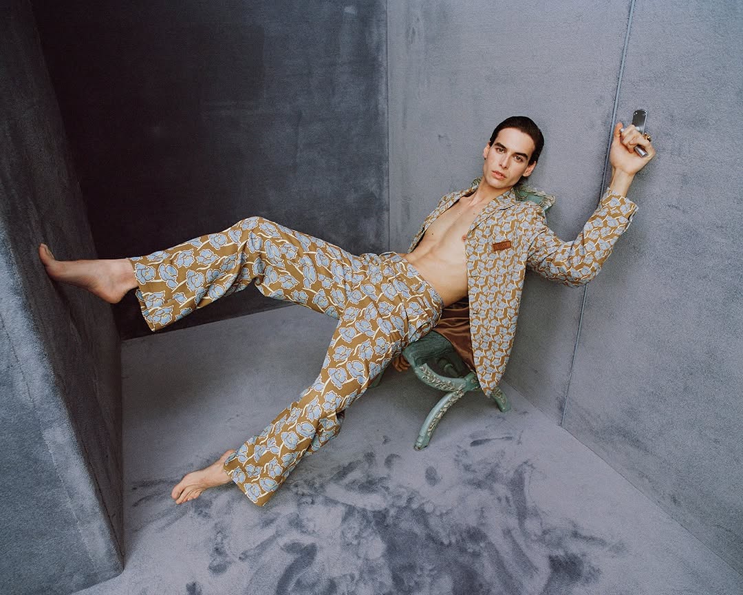 Man wearing a patterned suit and trousers seated in a grey studio corner for Versace