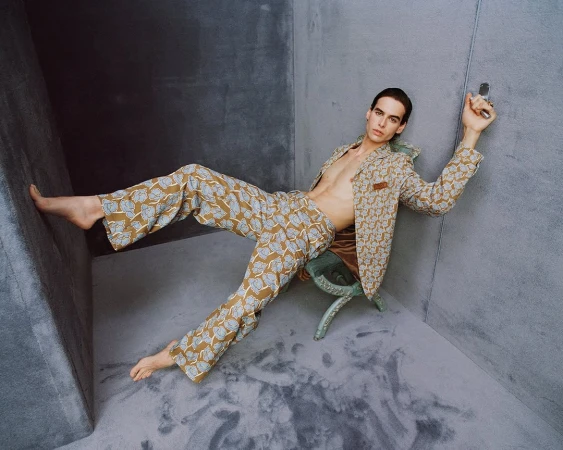 Man wearing a patterned suit and trousers seated in a grey studio corner for Versace