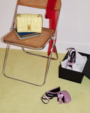 Yellow quilted handbag on a cane folding chair with purple platform sandals nearby for Versace Spring 2025 ad campaign.