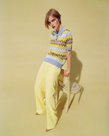 Model leaning against a chair wearing a chevron polo shirt and yellow trousers