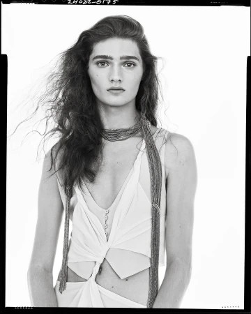 Monochrome portrait of a model with long dark hair wearing a sleeveless top and beaded necklace against a plain white background