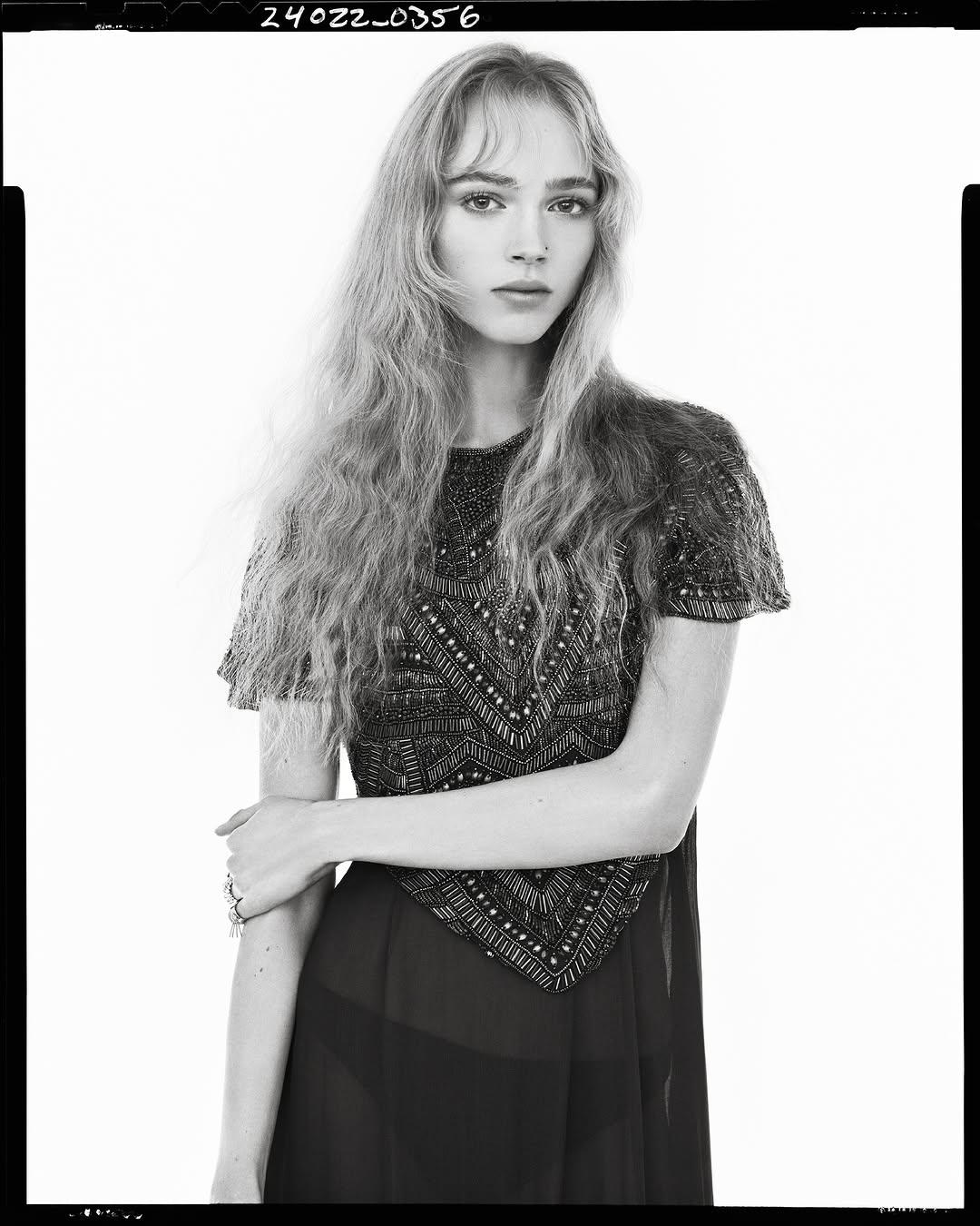 Model in embellished short-sleeve dress against a plain white studio background in a vertical monochrome fashion frame
