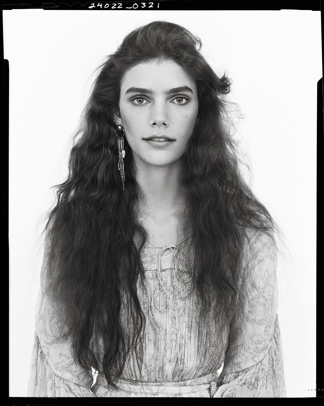 Portrait of a woman with long dark wavy hair wearing patterned dress against white studio background