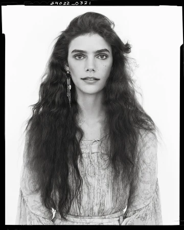 Portrait of a woman with long dark wavy hair wearing patterned dress against white studio background