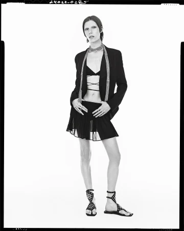 Model in black blazer and pleated mini skirt wearing strappy flat sandals against a white background for Zara