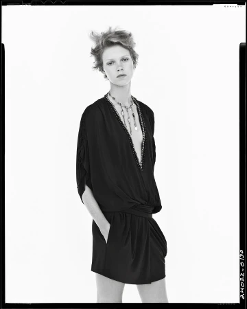 Model in black V-neck dress with layered necklace against white background for Zara Studio Spring 2025 campaign