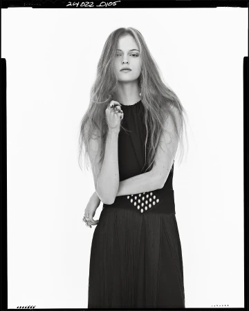 Model with long hair wearing a black sleeveless dress against a white studio background for Zara Spring 2025 campaign.