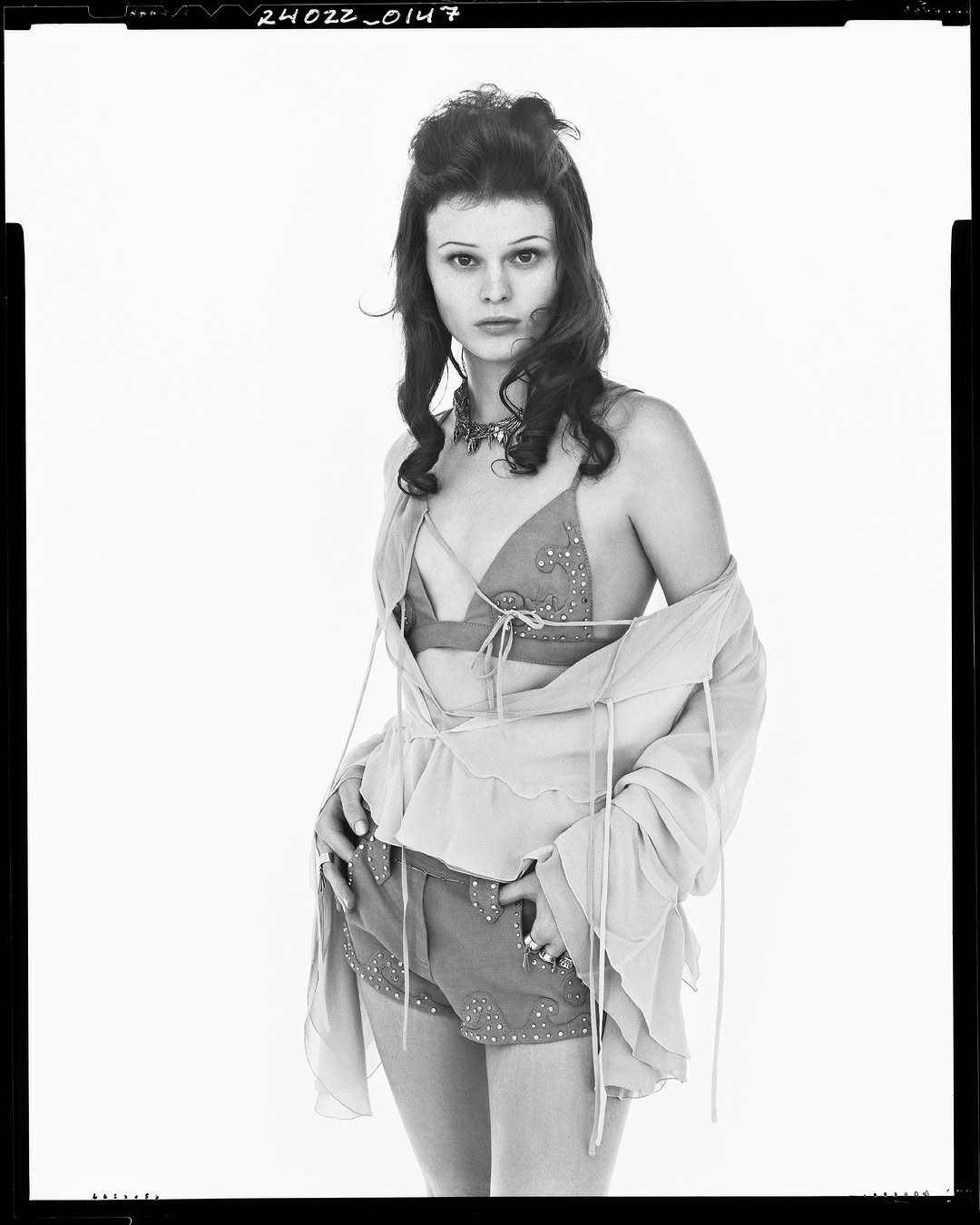 Model in layered summer outfit wearing decorated shorts against a white backdrop