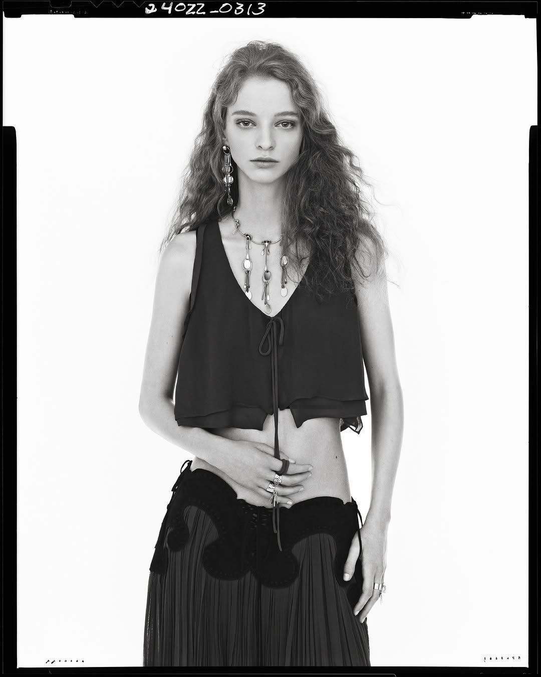 Model wearing a dark sleeveless top and dark skirt with ornate details against a plain white background in black and white.