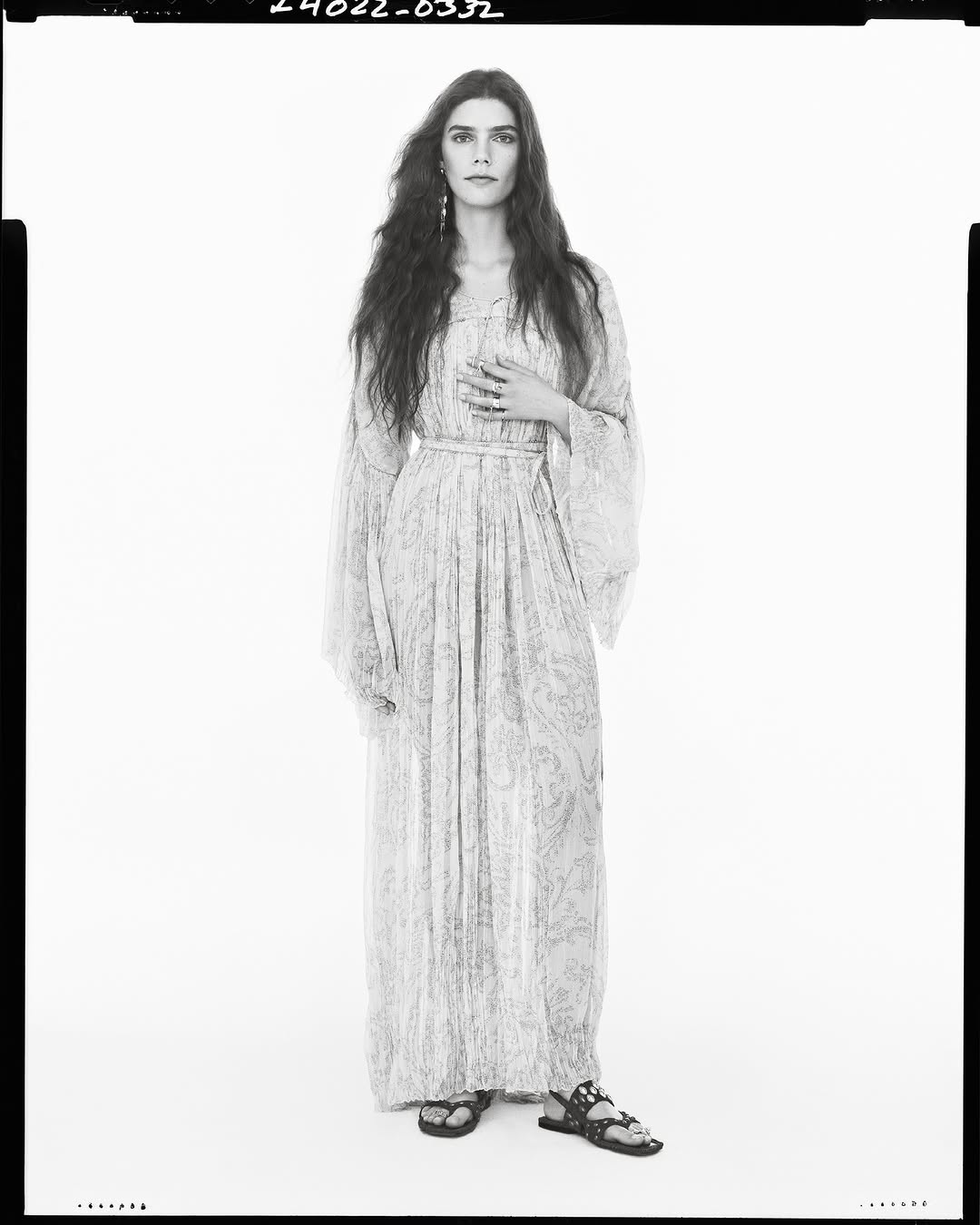 Model wearing a long patterned maxi dress standing against a plain light studio background.