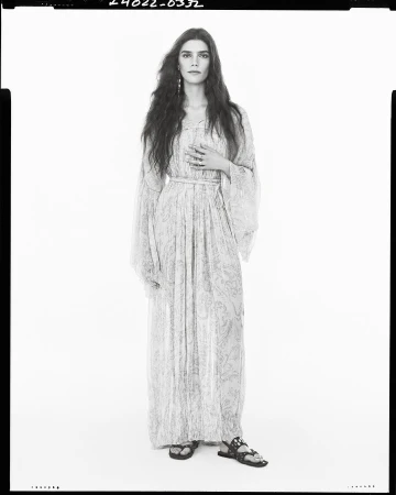 Model wearing a long patterned maxi dress standing against a plain light studio background.