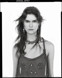 Portrait of a woman wearing a heavily embellished strap dress and ornate jewelry against a white studio background.