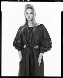 Model wearing dark bishop-sleeve dress with wide grommet belt against white seamless background