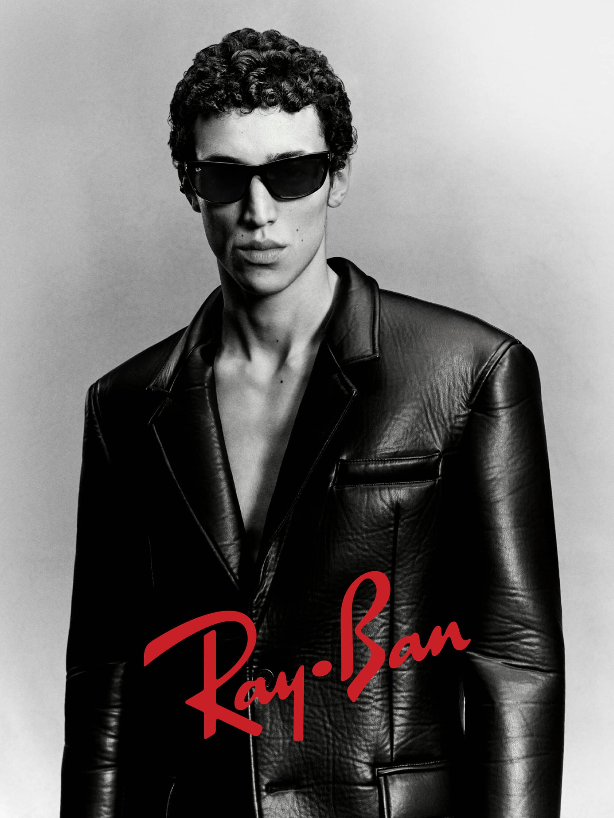 Man wearing sunglasses and a black leather jacket against a grey background with the red Ray-Ban logo