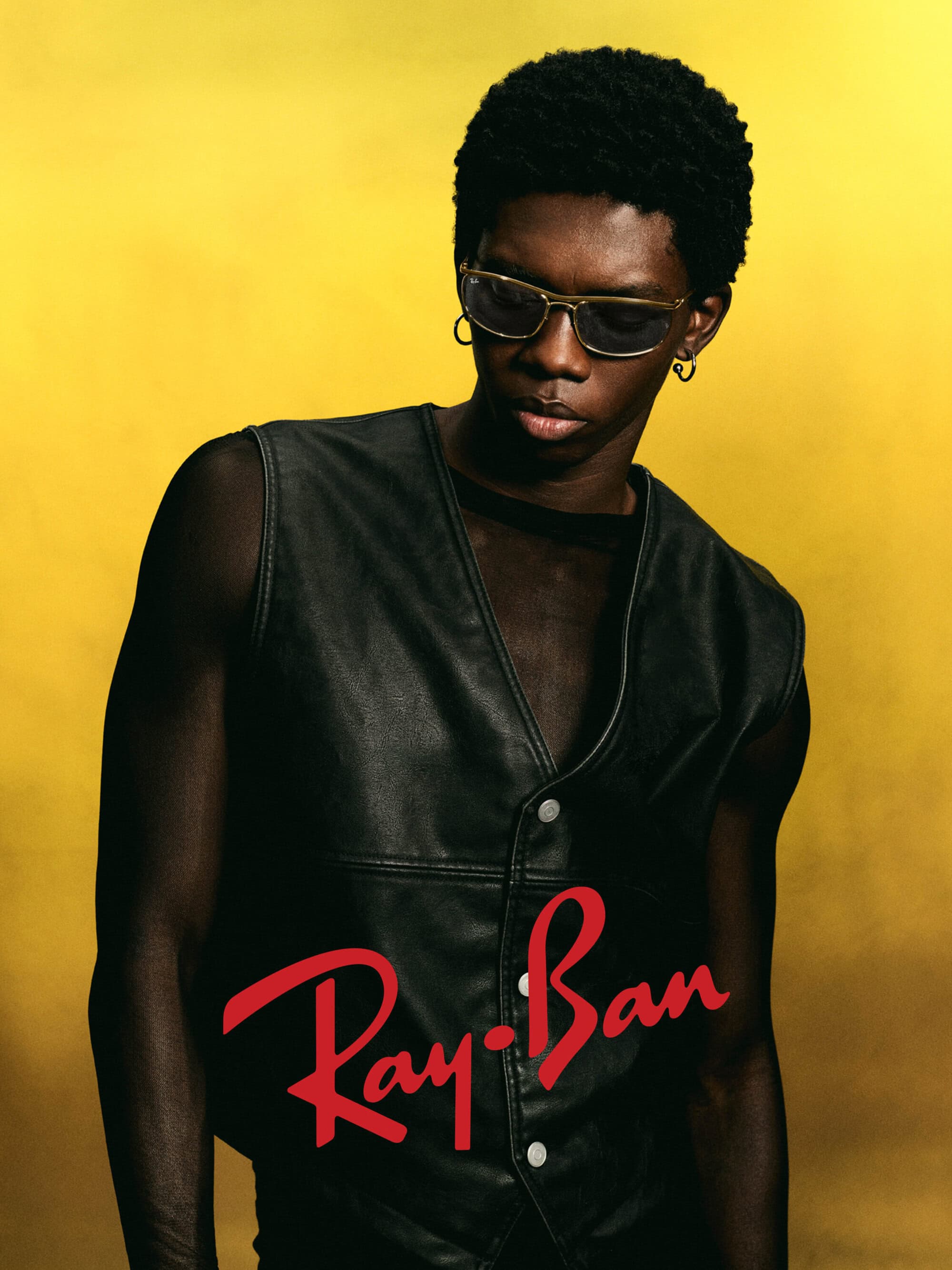 A Black man wearing sunglasses and a black leather vest poses against a bright yellow background for the Ray-Ban Icons ad campaign.