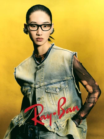 Model wearing black eyeglasses and a denim vest against a yellow background for the Ray-Ban 2025 campaign.