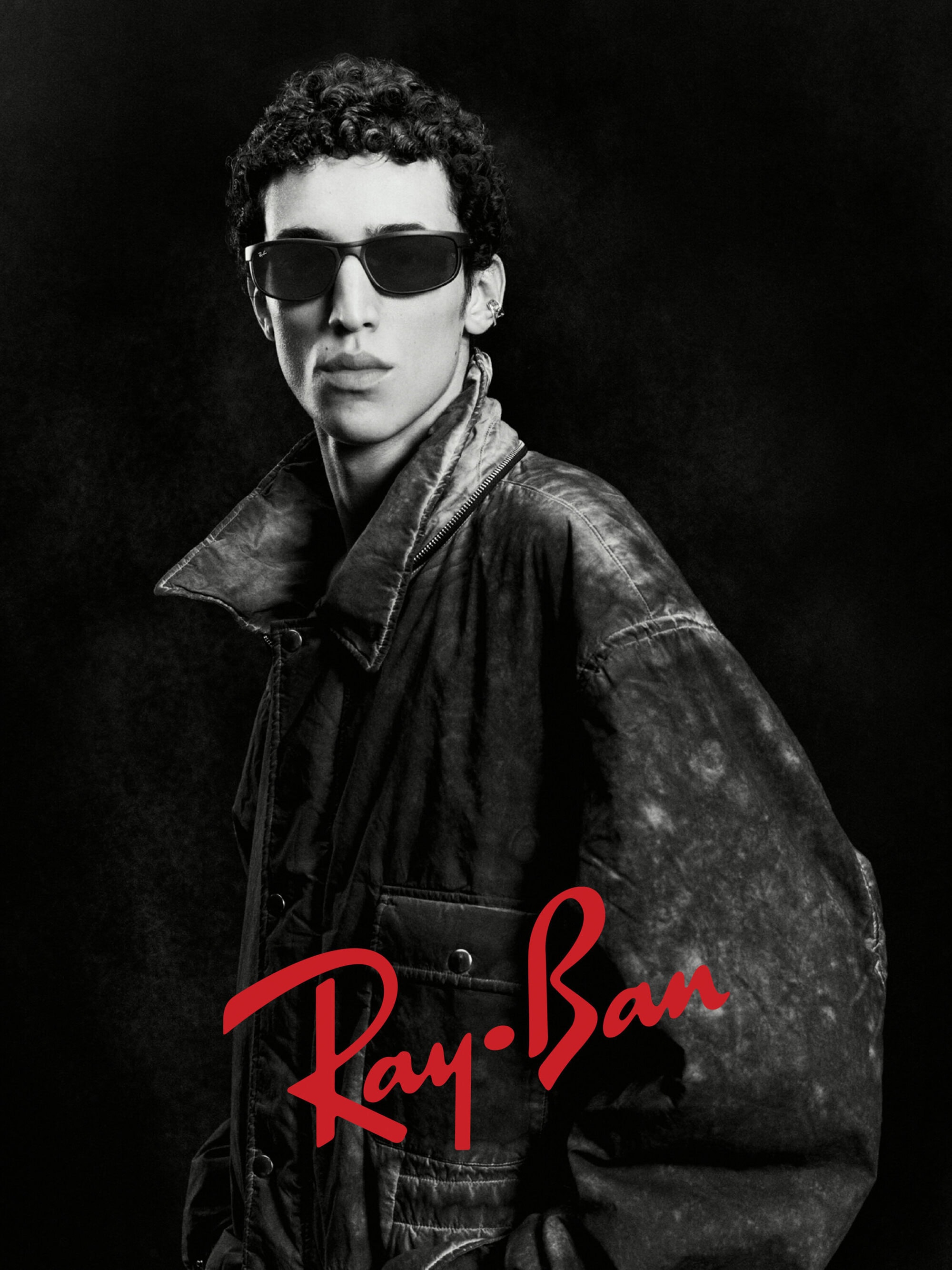 Model wearing dark sunglasses and a distressed dark jacket against a dark background for Ray-Ban