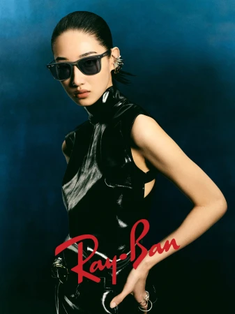 Model wearing dark sunglasses and black patent top against a moody blue background for Ray-Ban ad campaign