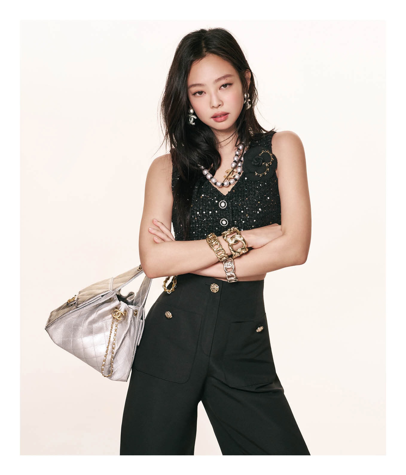 Jennie wearing a black tweed top and holding a quilted silver Chanel 25 handbag against a seamless white studio background