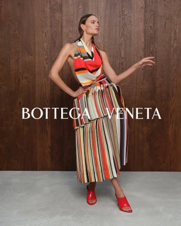 Model wearing a colourful striped halter top and pleated skirt against a wooden wall and concrete floor