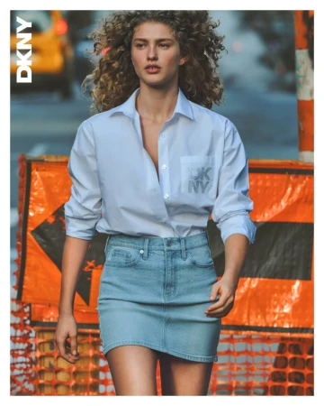 Model with curly hair wearing a white button-down shirt and denim skirt outdoors on a city street.