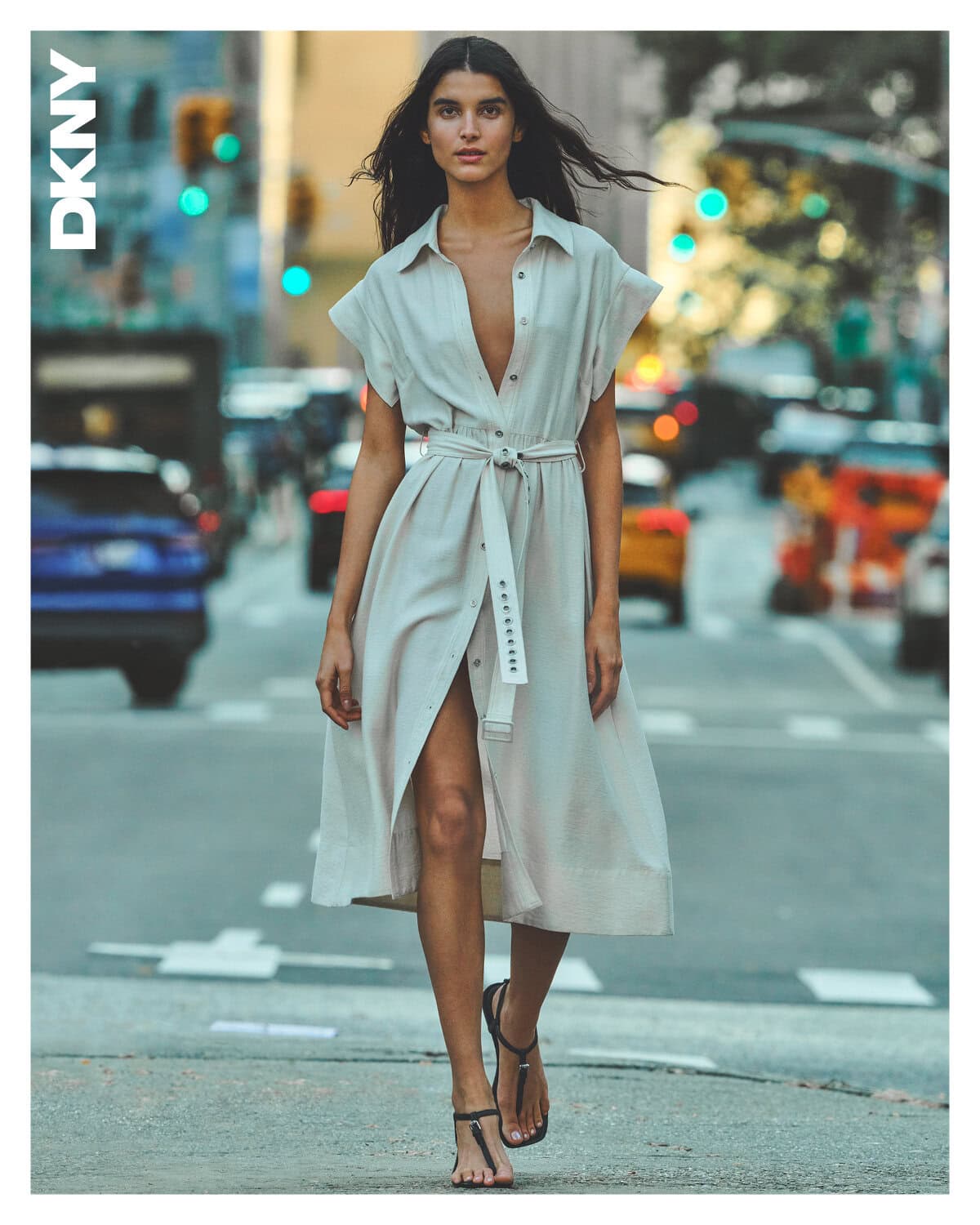 Model wearing a light beige belted midi shirt dress walking on a city street for DKNY Spring 2025 campaign