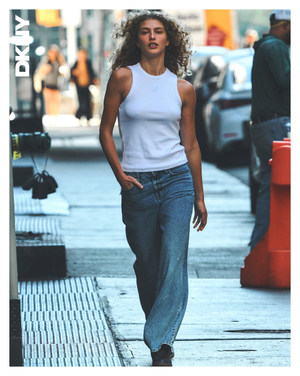 Model walking down a city sidewalk wearing a white tank top and blue jeans for the DKNY campaign