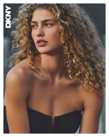 Portrait of a female model with long curly blonde hair wearing a strapless black top for DKNY Spring 2025 campaign.