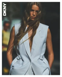 A female model wearing a white sleeveless blazer posing outdoors for the DKNY spring 2025 ad campaign.