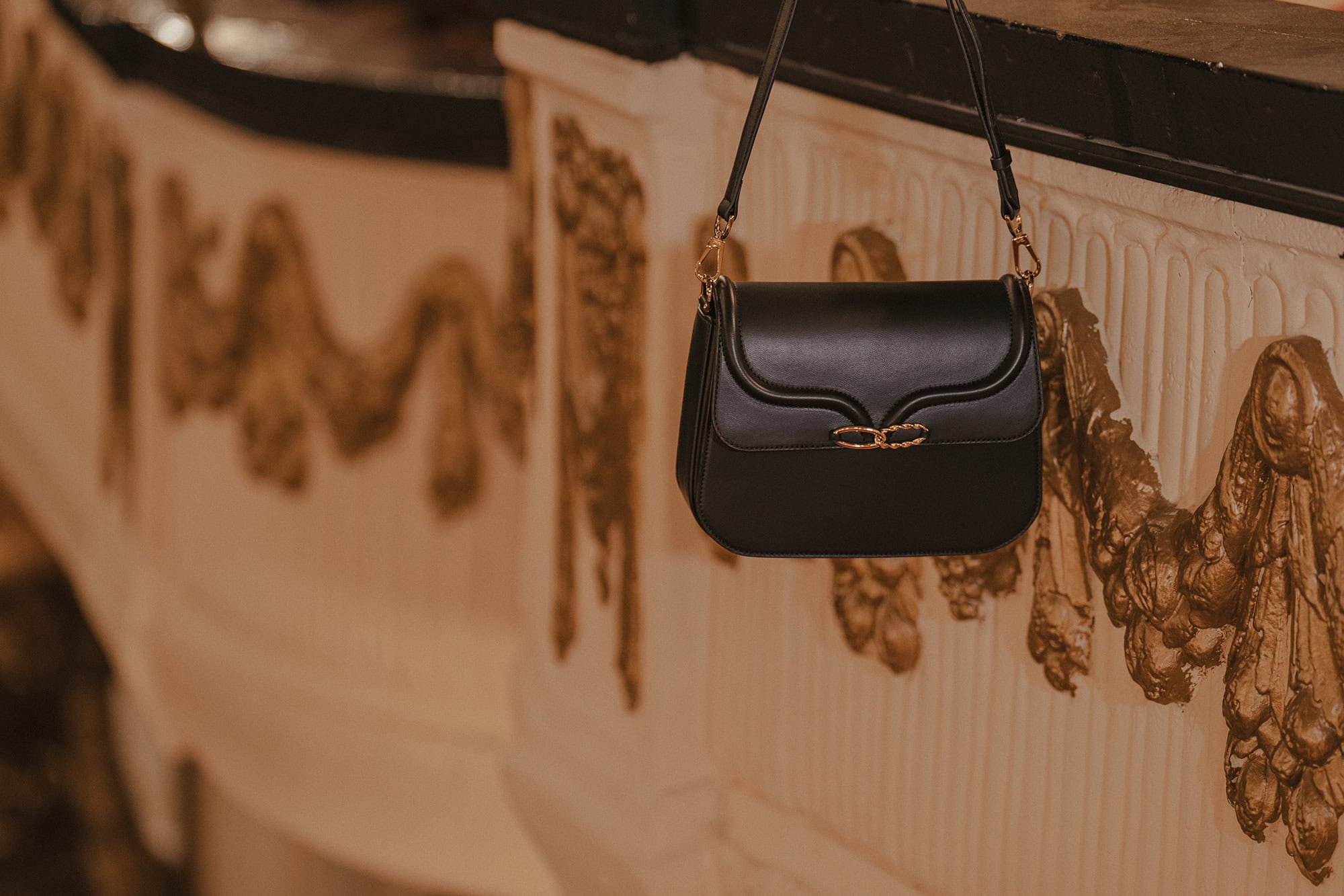 Black leather handbag with gold hardware hanging against ornate architectural wall details