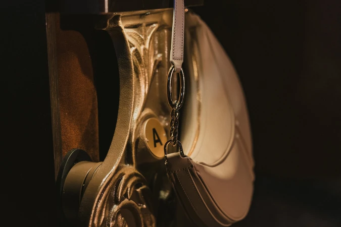 Beige leather shoulder bag hanging from an ornate gold architectural bracket for AGCF ad campaign.