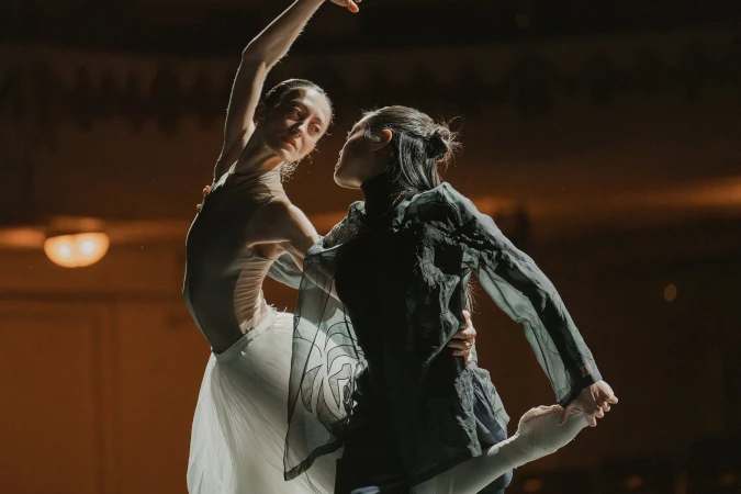 Two female ballet dancers performing in an atmospheric dark theater setting with dramatic spotlighting