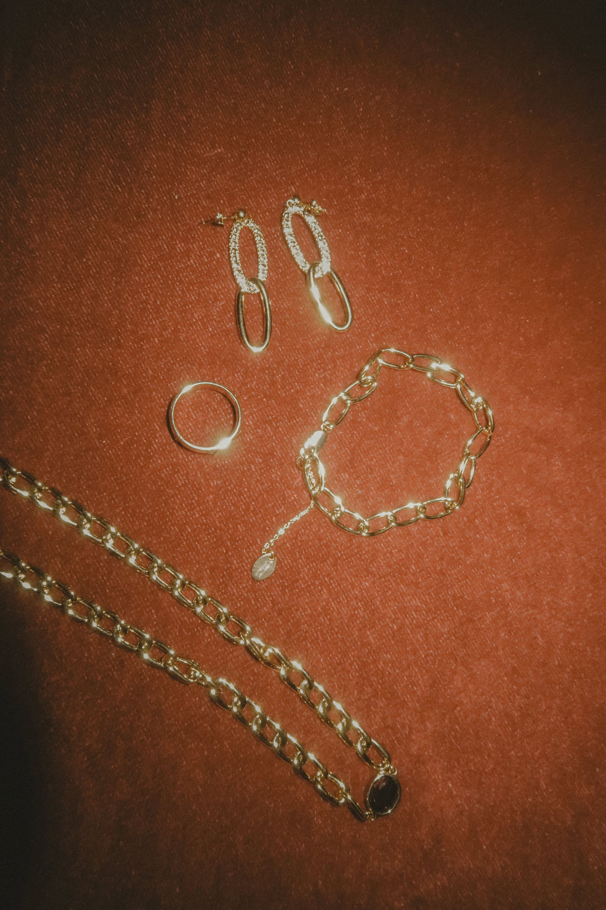 Collection of gold jewellery including a chain necklace, link bracelet, ring and drop earrings displayed on a dark velvet surface