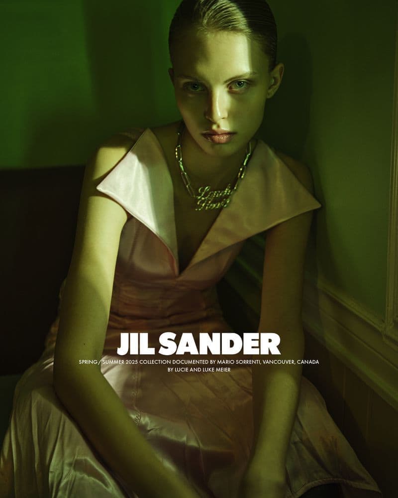 Model in a pale pink dress wearing a statement chain necklace against a moody green interior wall.