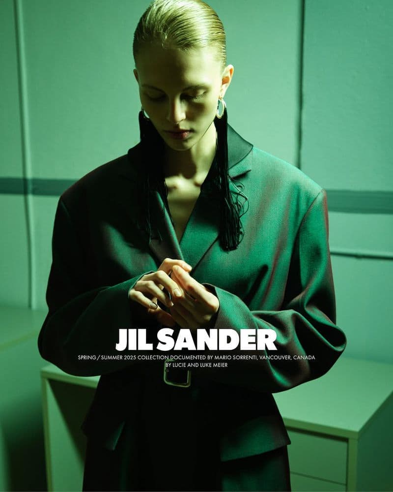 Model wearing dark green blazer jacket with slicked-back hair under moody green-toned lighting in an interior space