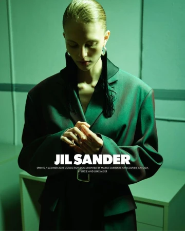 Model wearing dark green blazer jacket with slicked-back hair under moody green-toned lighting in an interior space