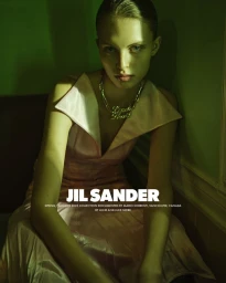 Model in a pale pink dress wearing a statement chain necklace against a moody green interior wall.