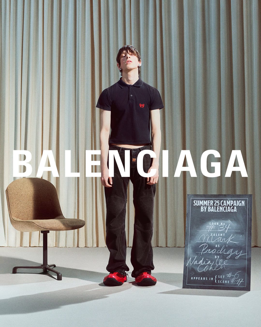 Model wearing black polo shirt and dark trousers standing against pleated curtains with Balenciaga typography overlay