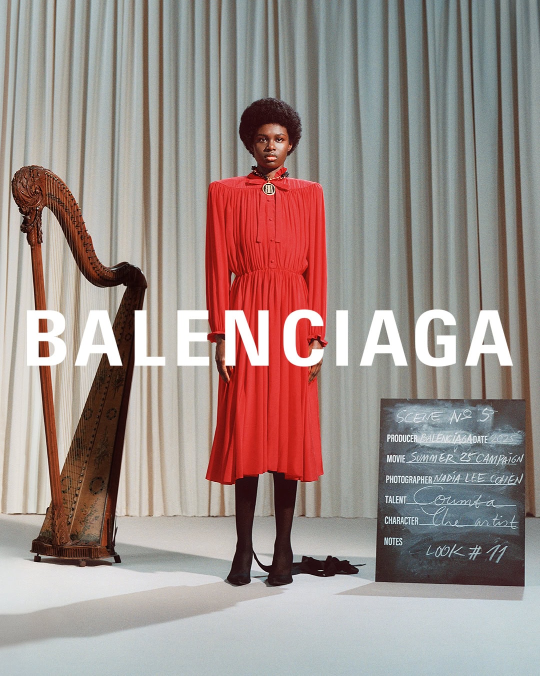 Model in a red dress standing before a harp and chalkboard with Balenciaga overlaid