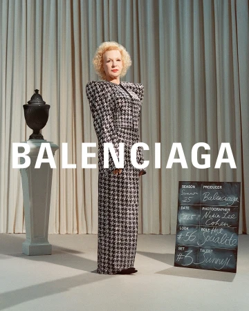 An older woman with blonde curly hair wearing a houndstooth gown standing in front of draped curtains with Balenciaga text overlay