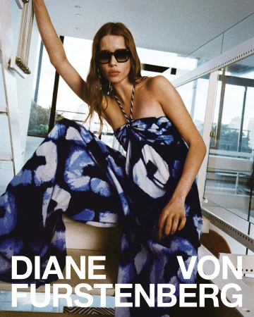 Model in blue patterned halter dress wearing sunglasses posing indoors on stairs for Diane von Furstenberg