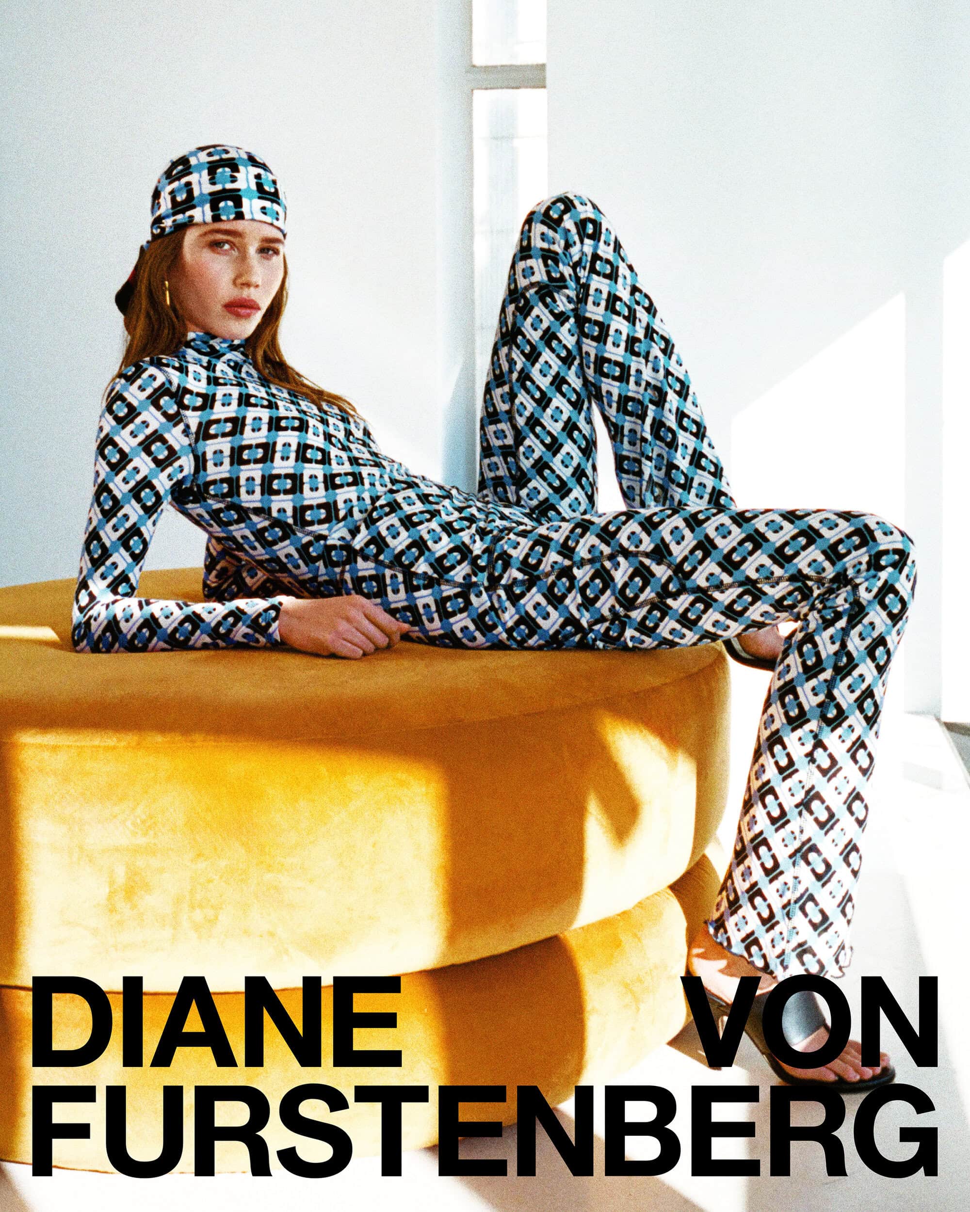 Model reclining on a yellow ottoman wearing a geometric patterned matching top, pants, and headscarf for Diane von Furstenberg.