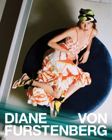Model in printed dress and patterned headscarf reclining on a dark blue circular lounge chair for Diane von Furstenberg