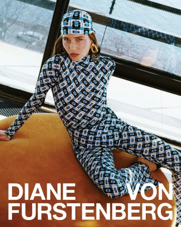 Model in blue patterned turtleneck and trousers with matching headscarf seated on an orange round ottoman